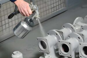 Worker applying paint to valve parts using a spray gun