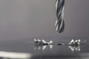 A metal drill bit makes holes in a steel billet with lubricating liquid on an industrial drilling machine